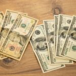 A collection of US dollar bills arranged on a wooden surface, showcasing currency denominations.