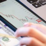 Close-up of a smartphone displaying stock market data over a dollar bill on a desk.