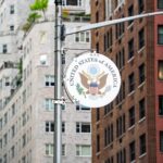 Street view of the US Embassy sign with New York City architecture in the background.