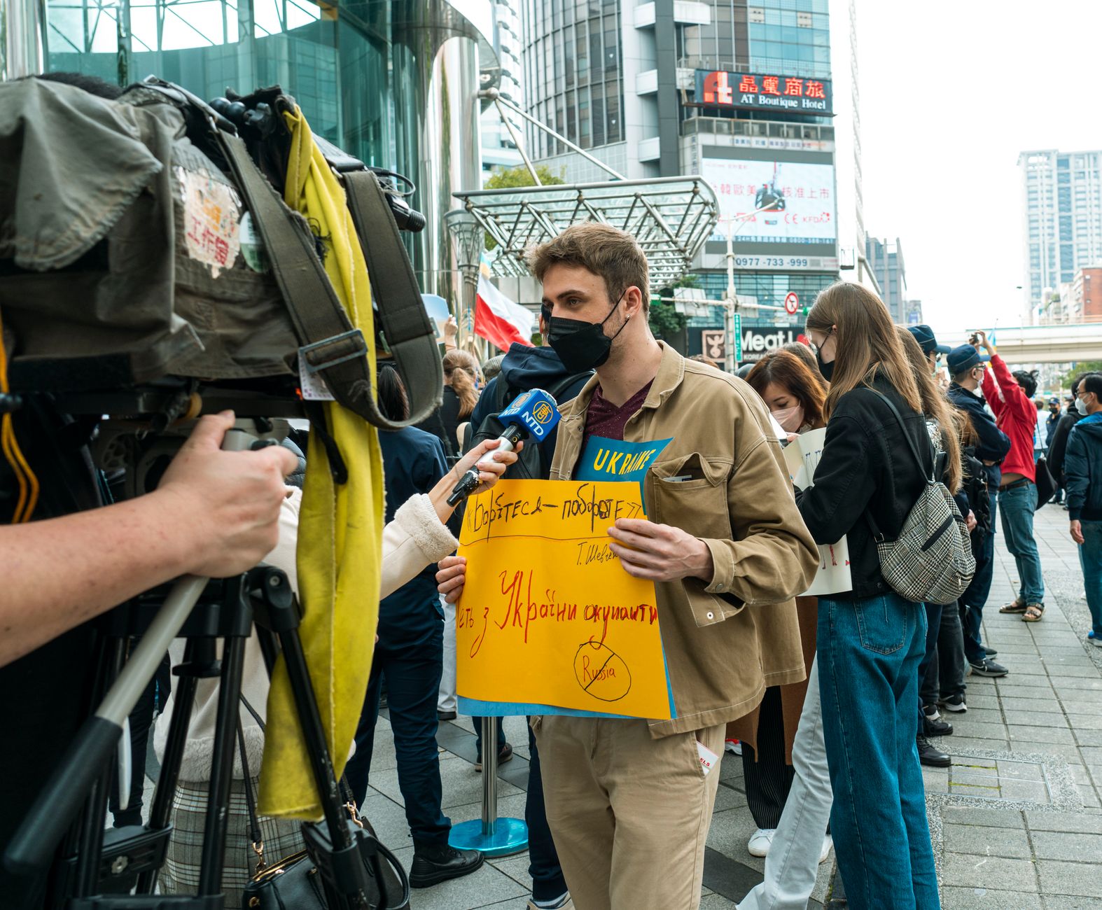 Young man holds protest sign during street demonstration against war, covered by media.