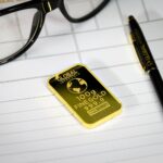 Gold bullion on notepad with eyeglasses and pen, symbolizing wealth and business planning.