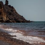 Waves crash on the rocky shore of Hormoz Island, Iran with clear blue skies.
