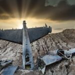 Dramatic sunset illuminating a crashed aircraft in a barren desert landscape.