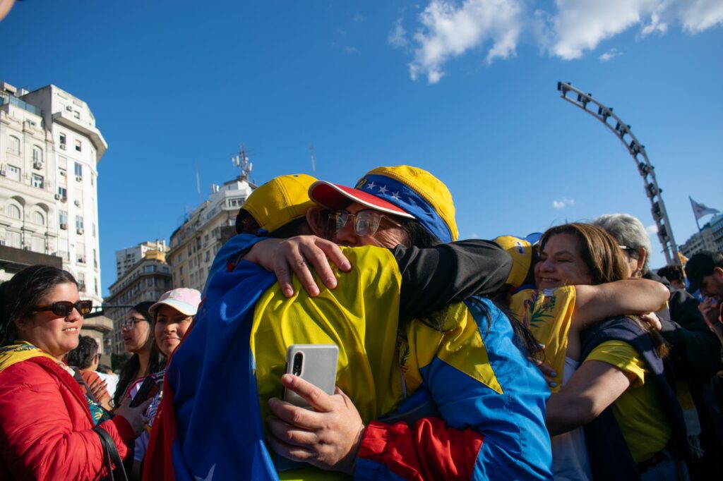 Group of Venezuelans embracing in a joyful celebration outdoors under a bright blue sky.