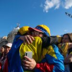 Group of Venezuelans embracing in a joyful celebration outdoors under a bright blue sky.