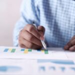 Close-up of hands analyzing colorful graphs, indicating business planning.