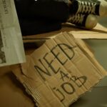 Close-up of a cardboard sign and newspaper depicting joblessness and unemployment.