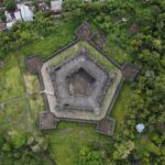 A top-down view of a historic fortified structure surrounded by greenery and adjacent buildings.