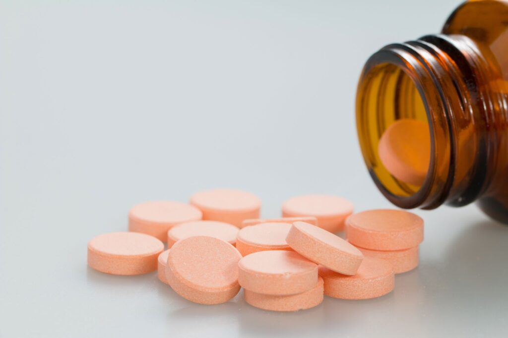Close-up image of orange tablets spilling from an amber bottle on a white surface.
