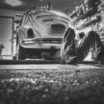 Mechanic working beneath a classic Volkswagen Beetle in a vintage garage setting.