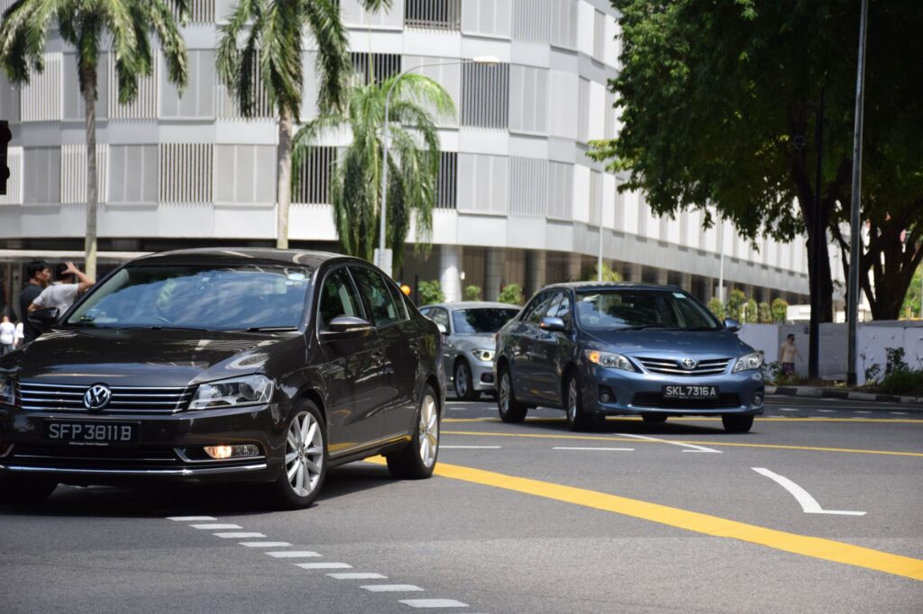 Busy city street in Singapore featuring several cars with modern building facade.