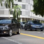 Busy city street in Singapore featuring several cars with modern building facade.