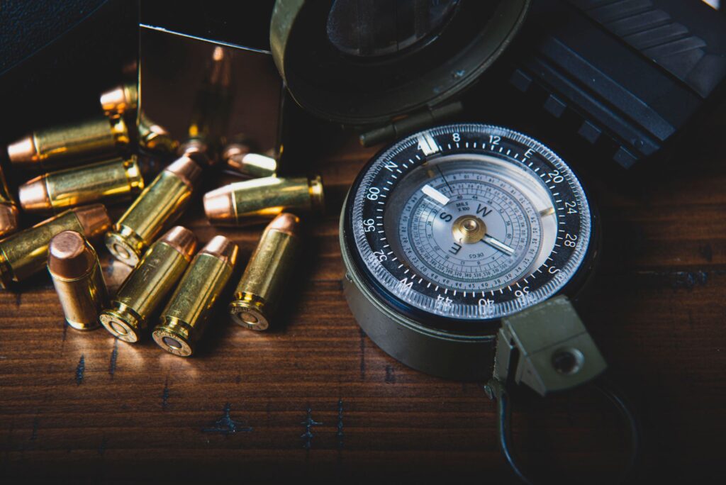 Close-up of brass bullets scattered around a vintage compass on a wooden surface, conveying exploration.