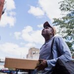 Man delivering a package in a city neighborhood, looking up at the building.