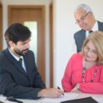 Senior couple signing real estate documents with an agent in a modern office setting.