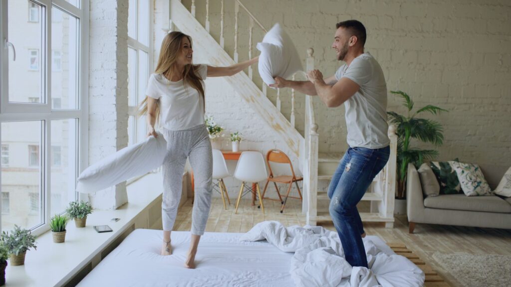 Happy young couple having a playful pillow fight in a cozy living room.