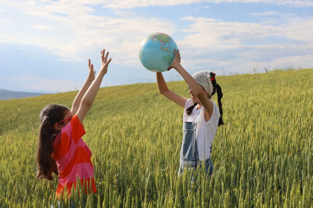 Joyful kids holding an earth globe in a lush wheat field, symbolizing global unity.