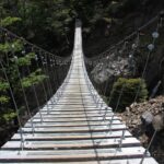 Dramatic view of a wooden suspension bridge stretching through a forested landscape.