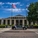 Government building facade with flags and police car in front on a sunny day.