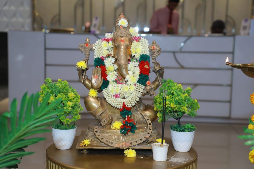 Intricately decorated brass Ganesha statue adorned with vibrant flowers, set indoors for a traditional feel.