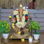 Intricately decorated brass Ganesha statue adorned with vibrant flowers, set indoors for a traditional feel.