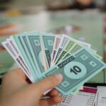 Close-up of a hand holding Monopoly money with board game in the background.