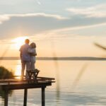 A senior couple embraces on a wooden dock at sunset, exuding tranquility and affection.