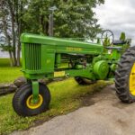 A green vintage John Deere tractor parked near a lake in Hawkesbury, Ontario, Canada.