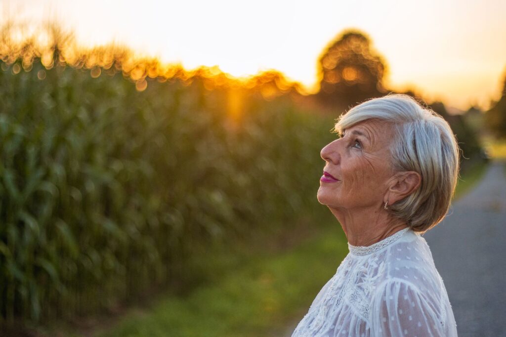 Elderly woman admiring the sunset in a lush park, highlighting relaxation and natural beauty.