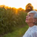Elderly woman admiring the sunset in a lush park, highlighting relaxation and natural beauty.