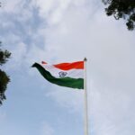 Low angle shot of the Indian national flag on a flagpole with a clear blue sky.