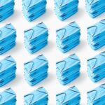 Multiple stacks of blue medical face masks arranged on a white background, emphasizing cleanliness and healthcare.