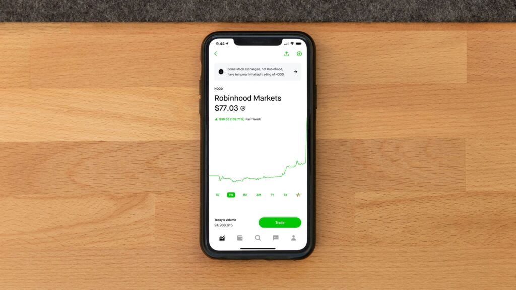 Stock trading app on smartphone displaying Robinhood Markets price on wooden desk.