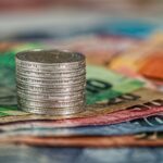 A stack of coins on top of various colored banknotes, symbolizing finance and currency.