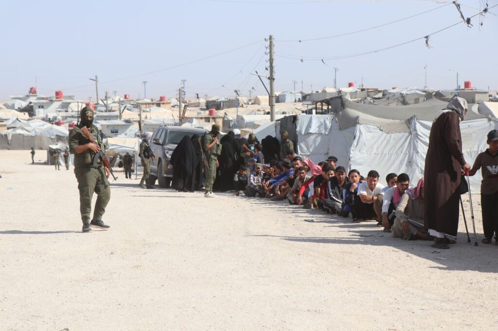 Refugees in al-Hol camp, Syria, guarded by soldiers, highlighting humanitarian crisis.