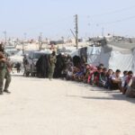 Refugees in al-Hol camp, Syria, guarded by soldiers, highlighting humanitarian crisis.